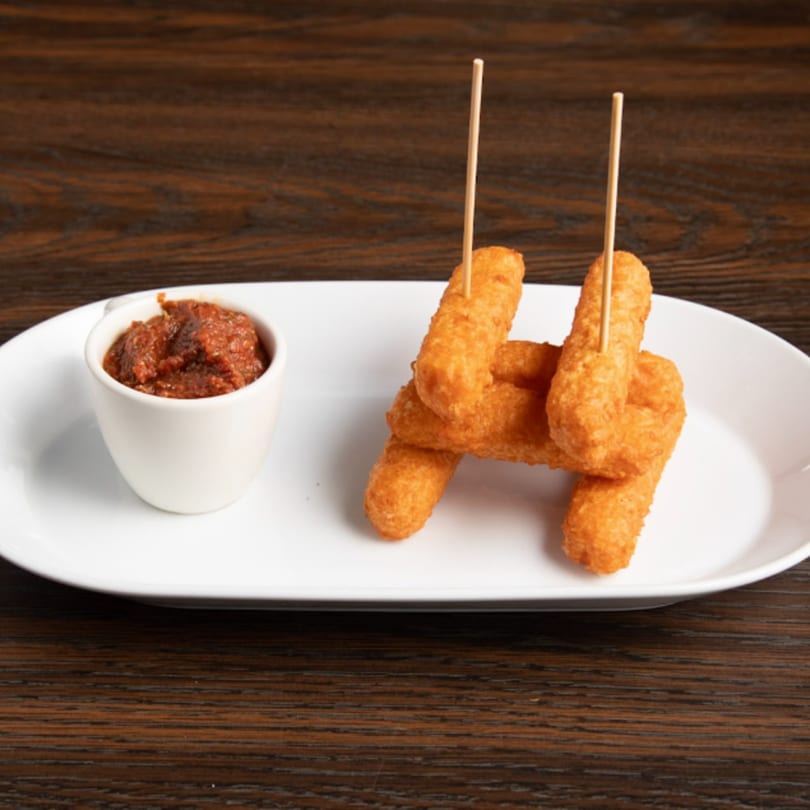 Golden-brown mozzarella sticks with toothpicks, served with a side of marinara sauce on a white plate.