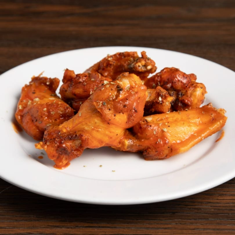 A plate of Game Time Sports Bar's buffalo wings, coated in a rich, spicy sauce and seasoning.