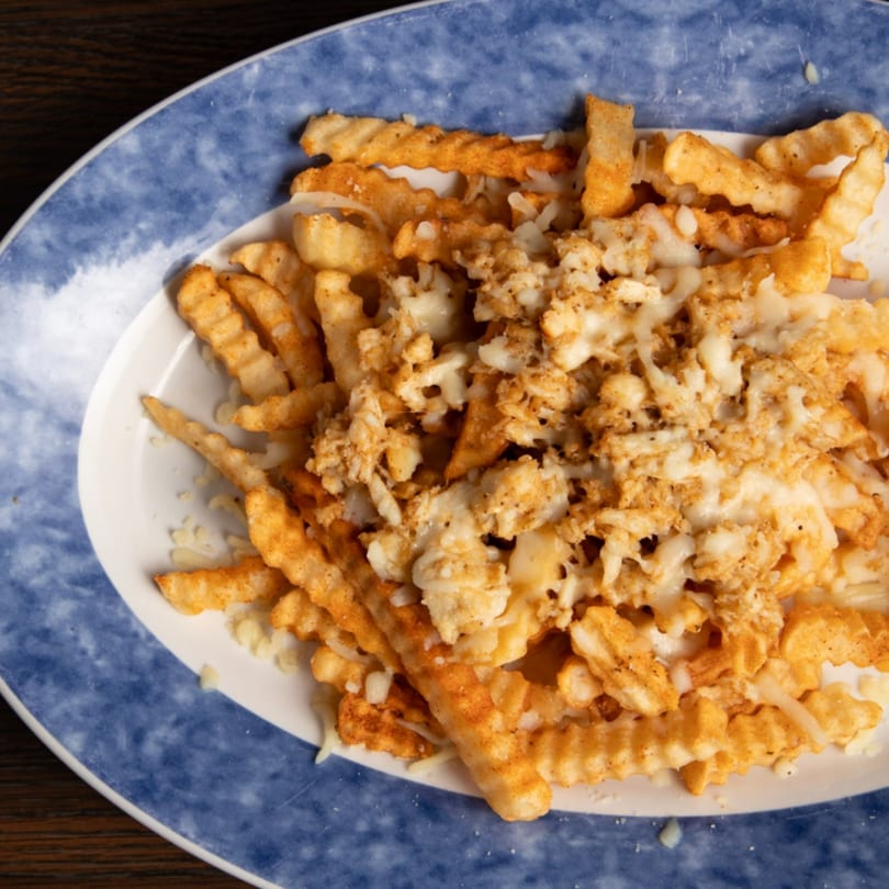 Close-up of crispy crinkle-cut fries topped with melted cheese and seasoning on a blue and white plate.