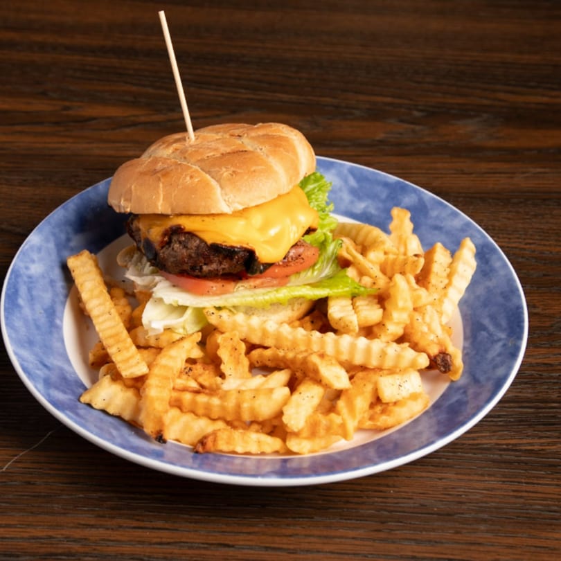 Cheeseburger with lettuce, tomato, and crinkle-cut fries on a blue and white plate.