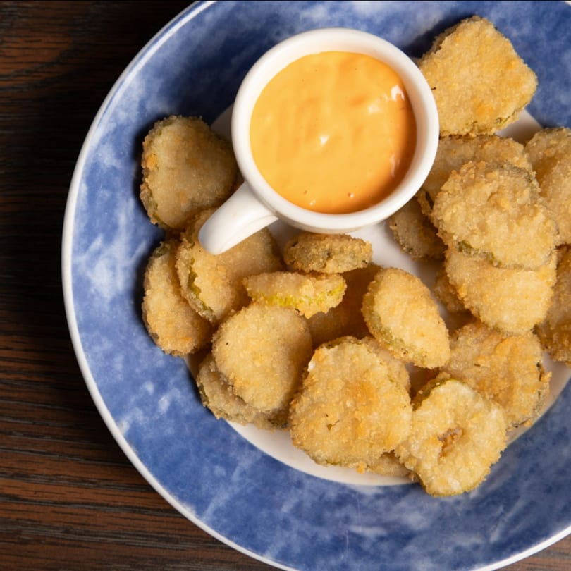 A blue and white plate filled with golden-brown fried pickles and a side of orange dipping sauce.